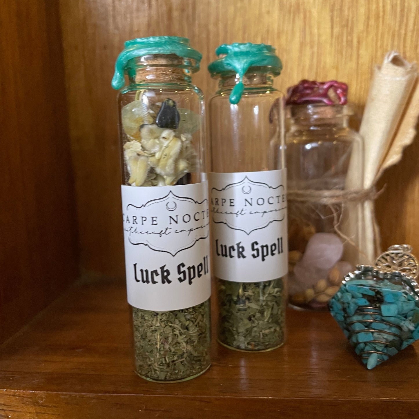 Two small glass jars labeled 'Luck Spell' on a wooden surface with decorative items.