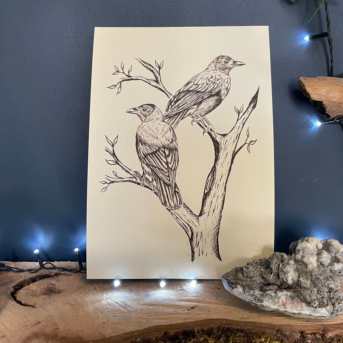 Illustration of two birds on a branch on a piece of paper, placed against a dark background with decorative elements.