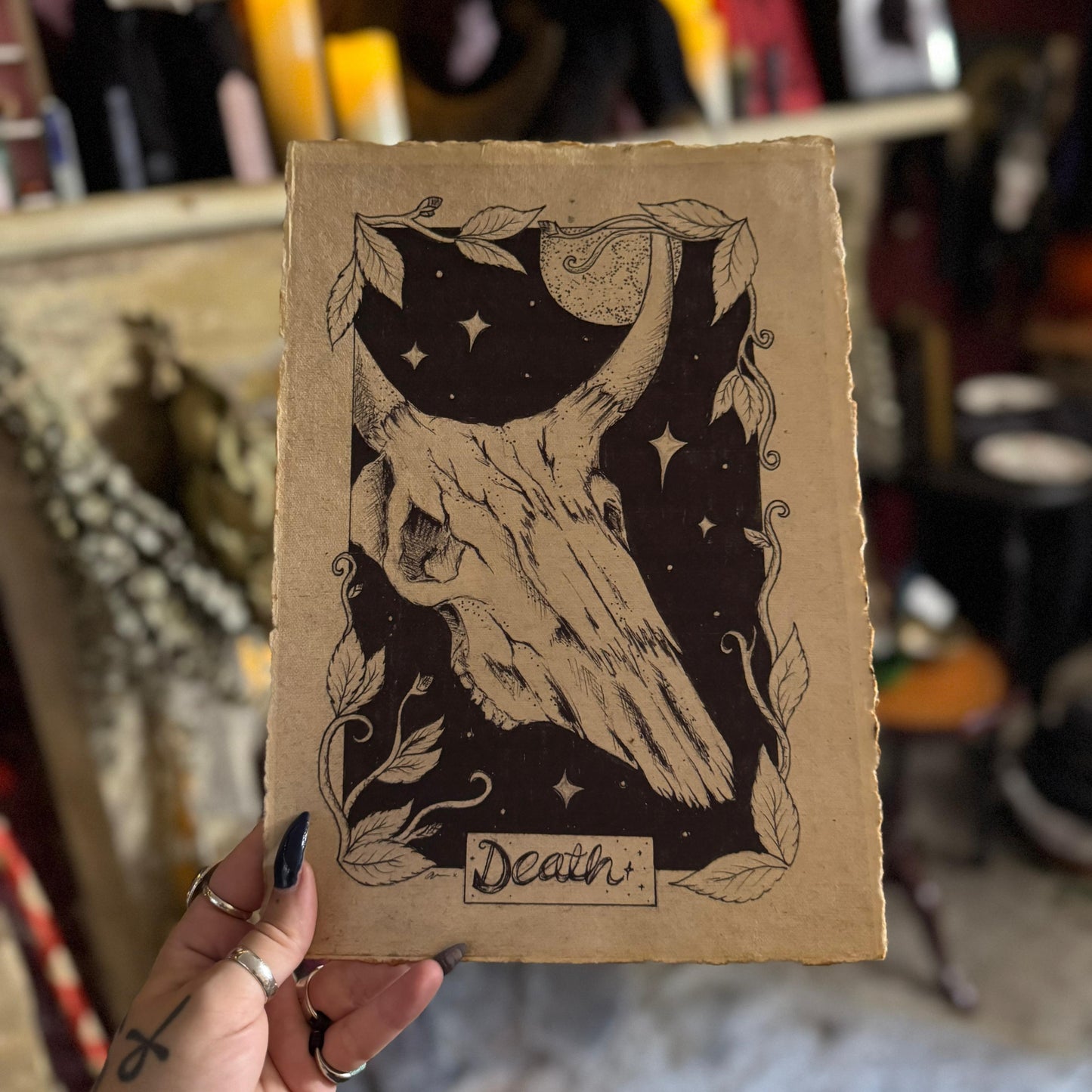 Card with a skull design and 'Death' text held by a person in a blurred indoor setting.