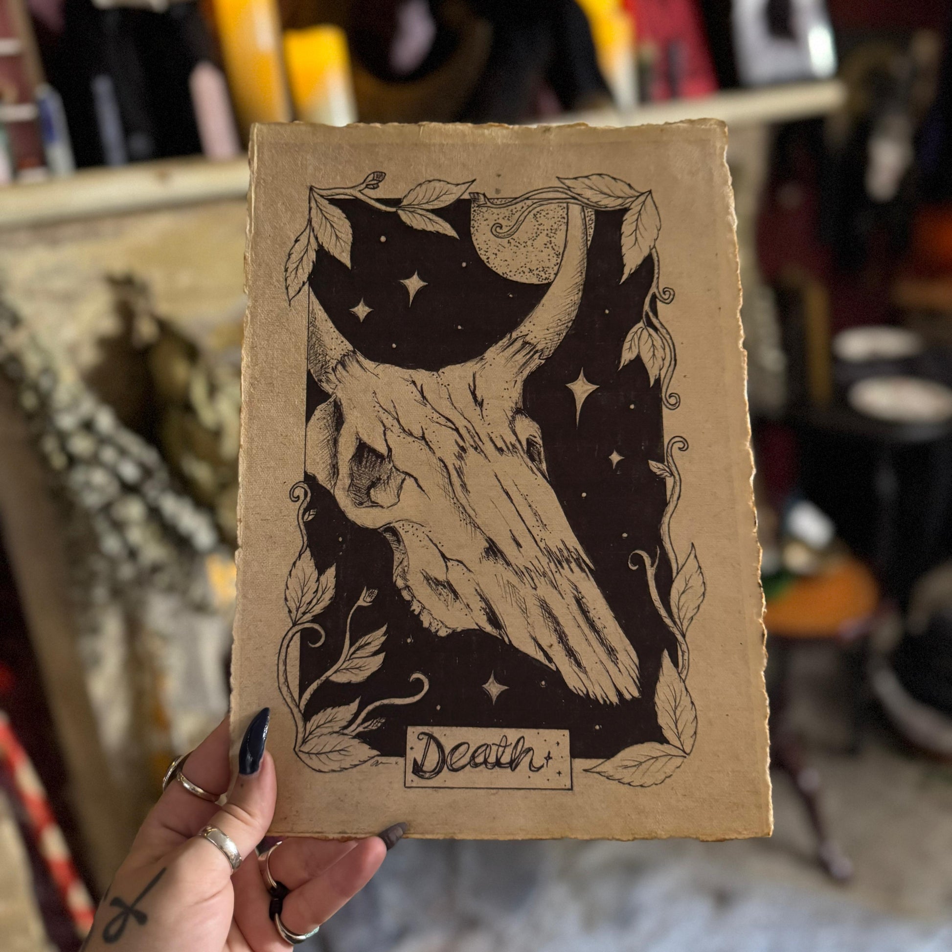 Card with a skull design and 'Death' text held by a person in a blurred indoor setting.