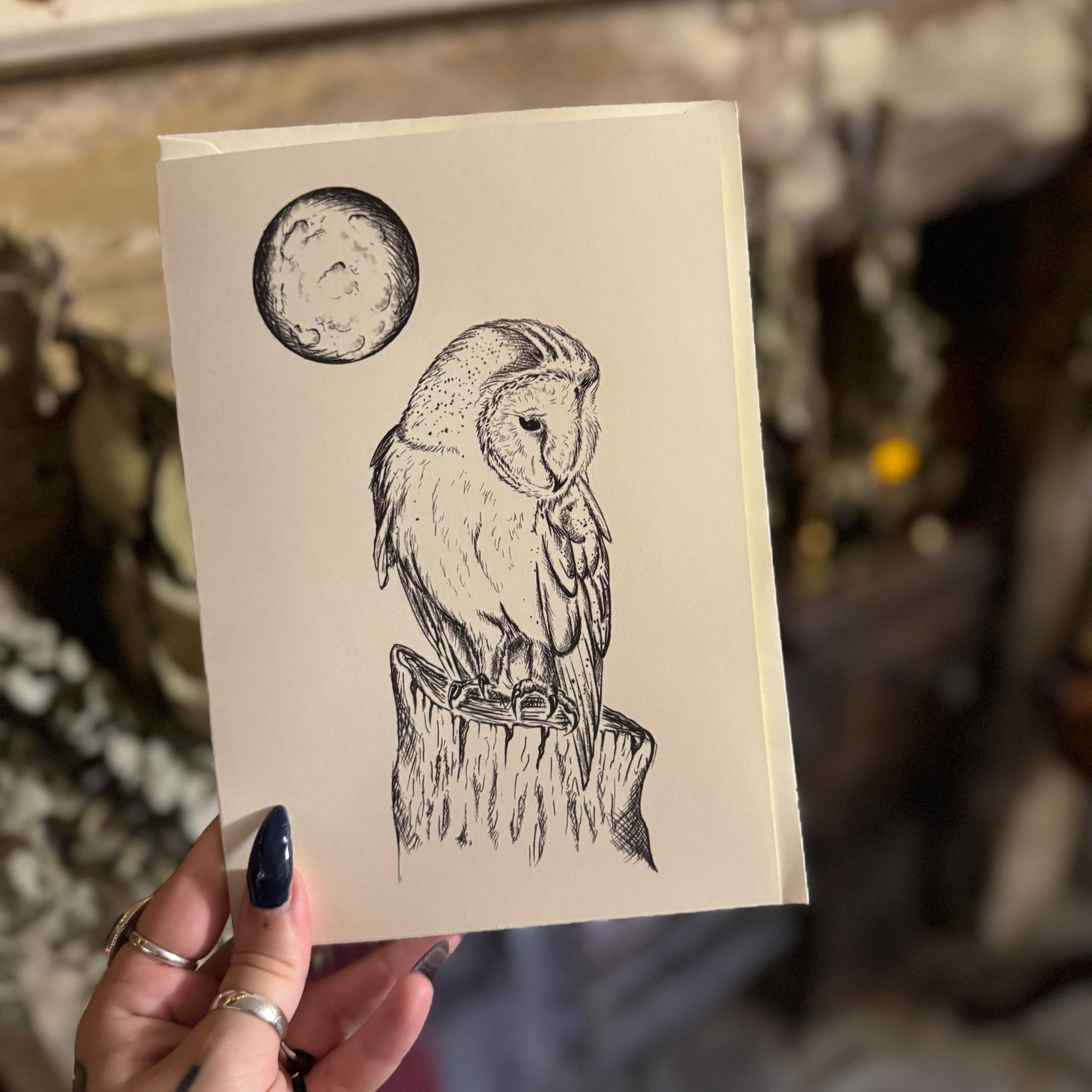 Hand holding a card with an owl illustration and moon design.