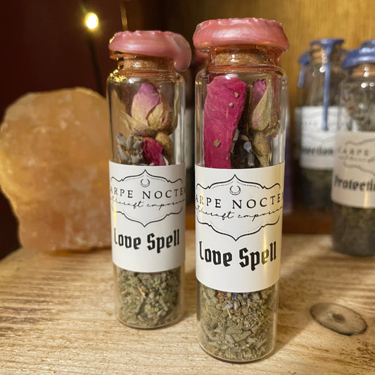 Two small glass bottles with herbs and flowers on a wooden surface