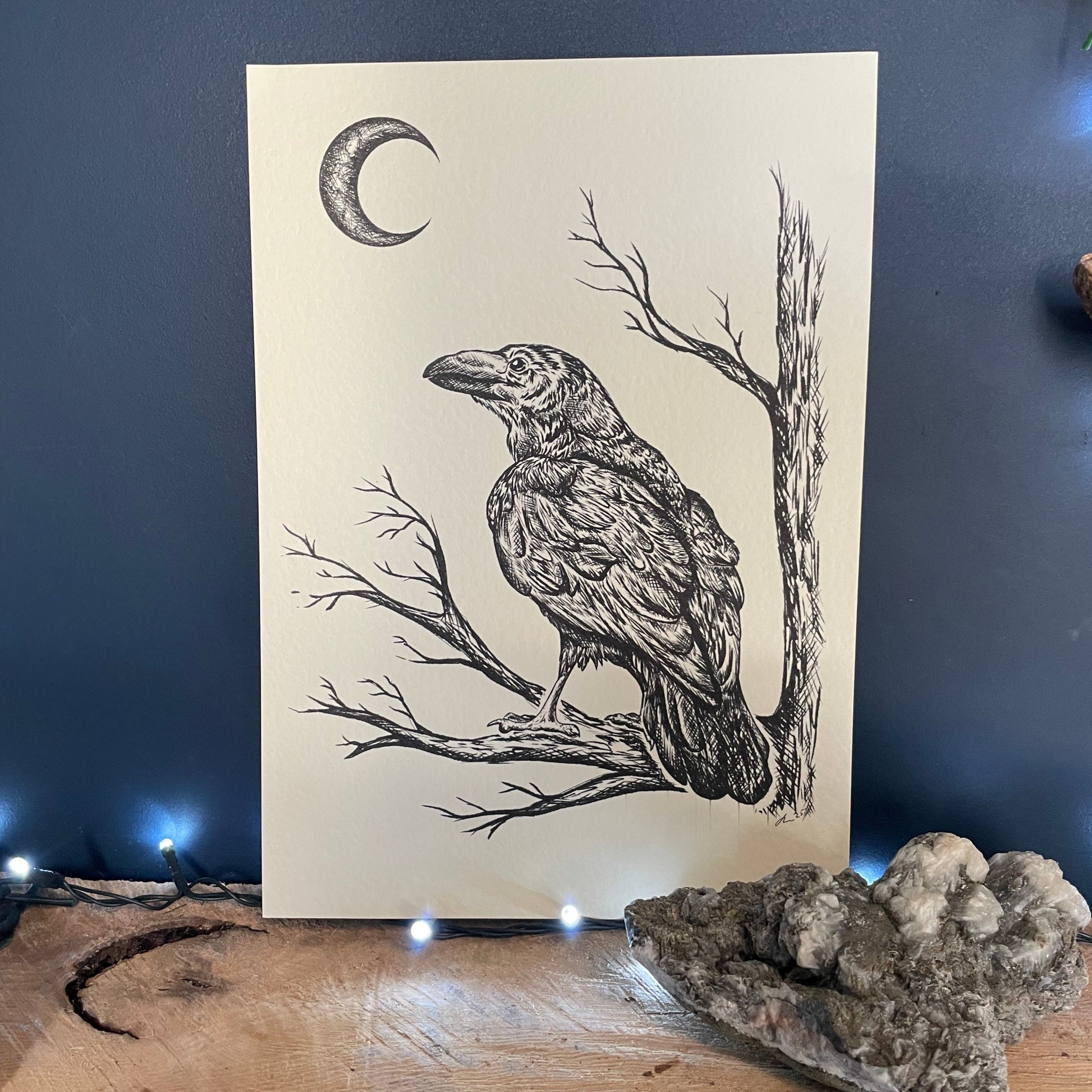 Illustration of a bird on branches with a moon on a piece of paper, placed on a textured surface.