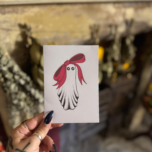 Hand holding a card with a ghost with red hair design against a blurred background