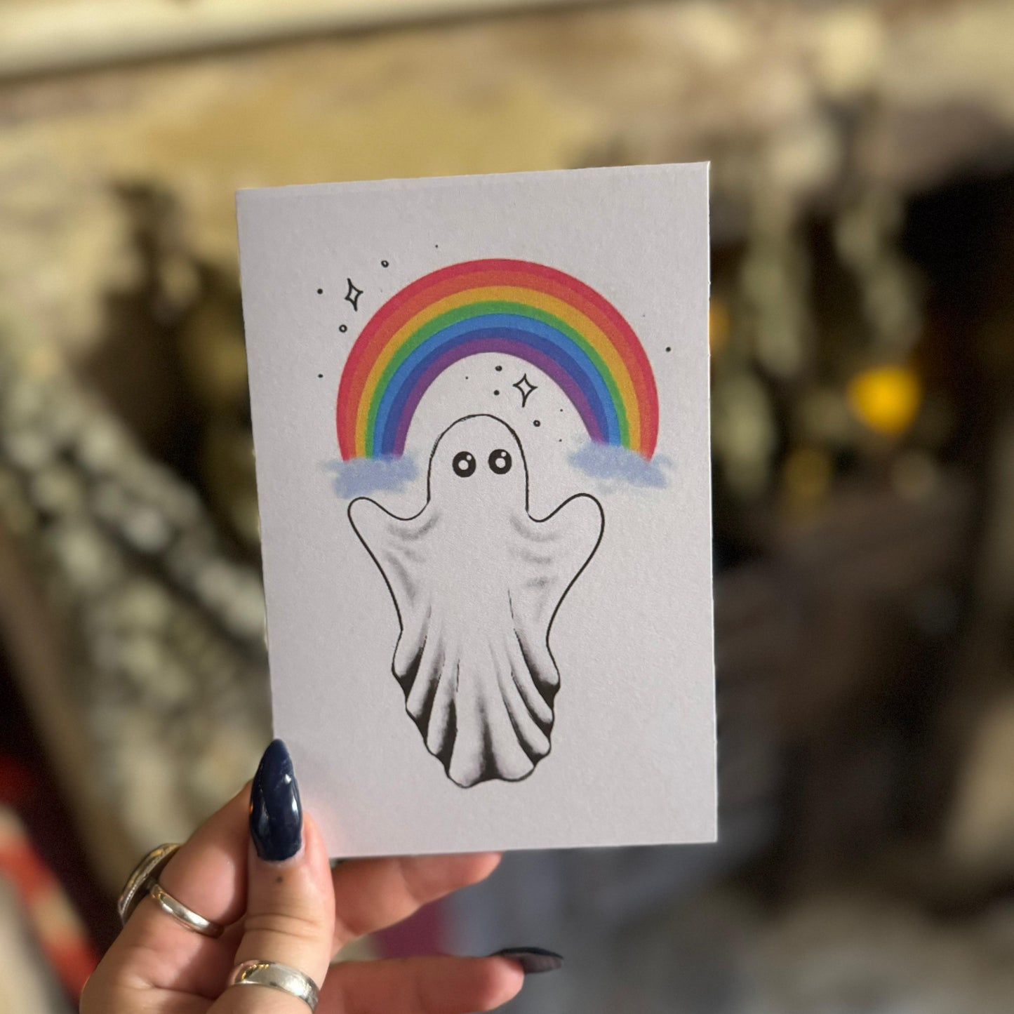 Hand holding a card with a ghost and rainbow illustration.