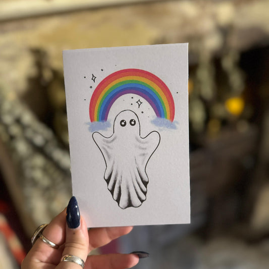 Hand holding a card with a ghost and rainbow illustration.